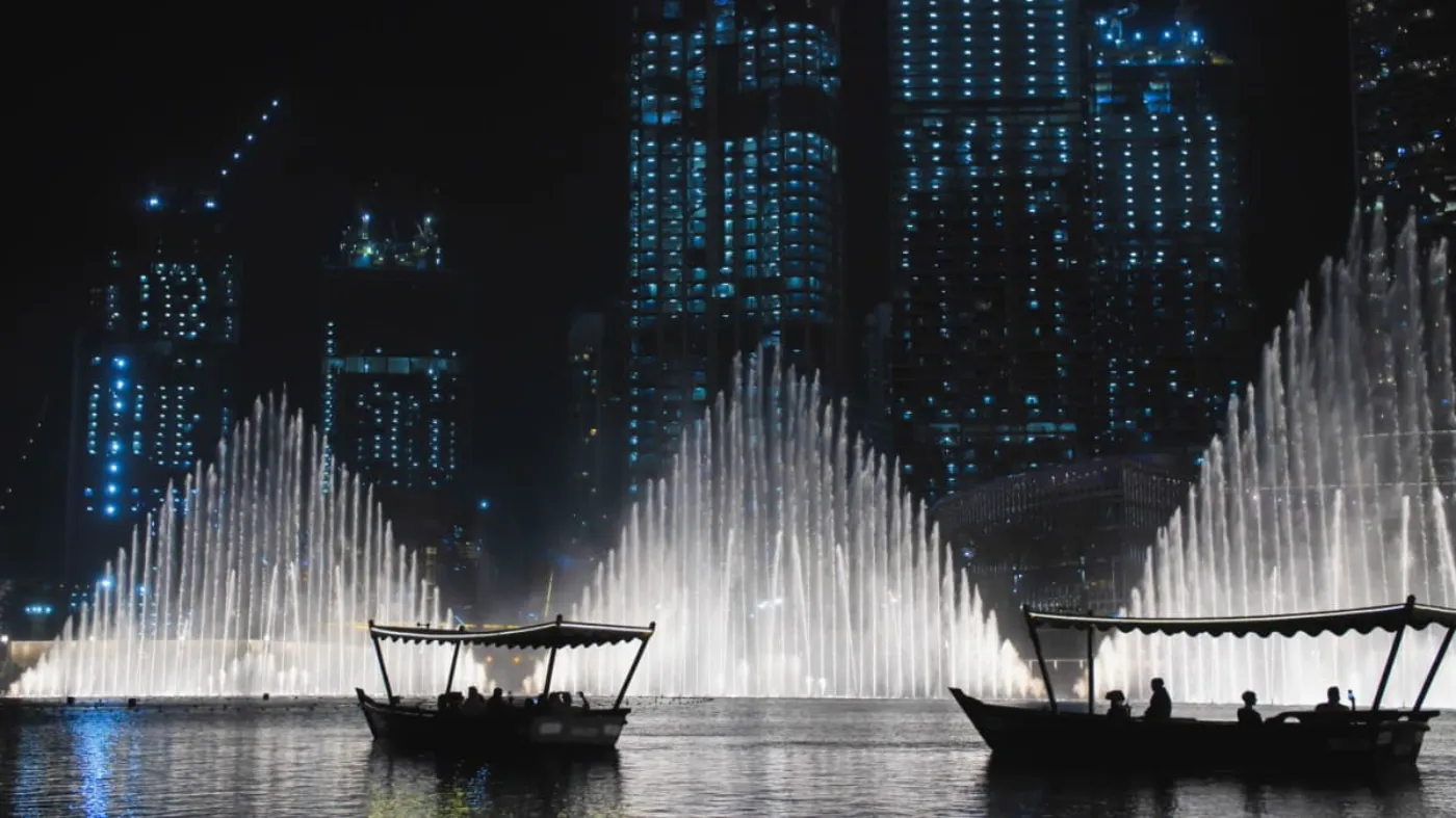 Deux bateaux avec en arrière plan un spectacle de jets de fontaine, de nuit au Burj Park à Dubaï